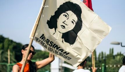 peserta aksi buruh mengibarkan bendera Marsinah dalam aksi buruh di Indonesia